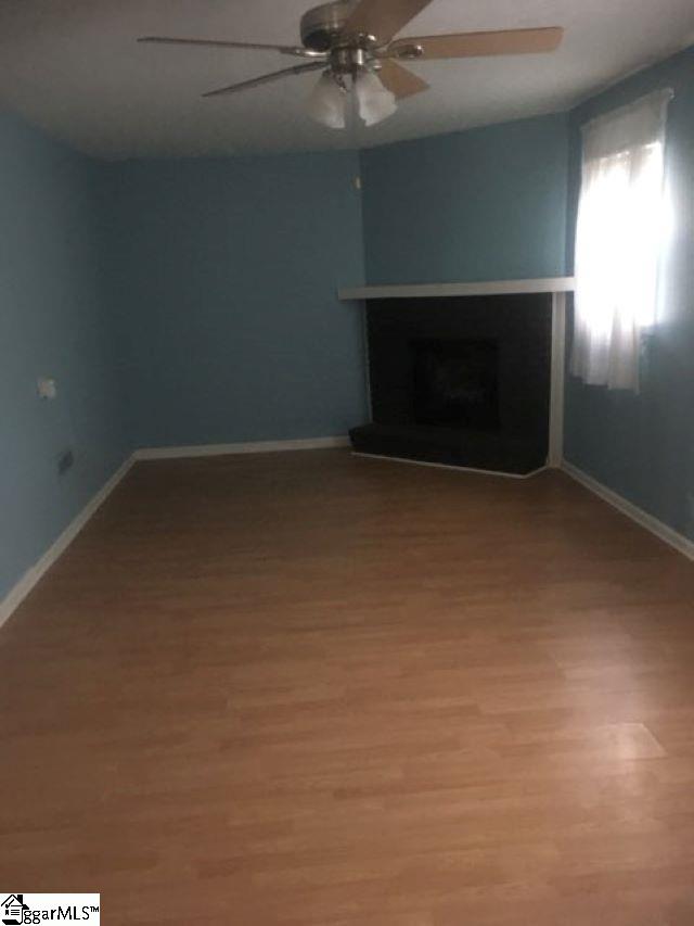 413 S Florida Ave, Greenville, SC 29611 - unfurnished living room with a ceiling fan, light wood-type flooring, a fireplace with raised hearth, and baseboards