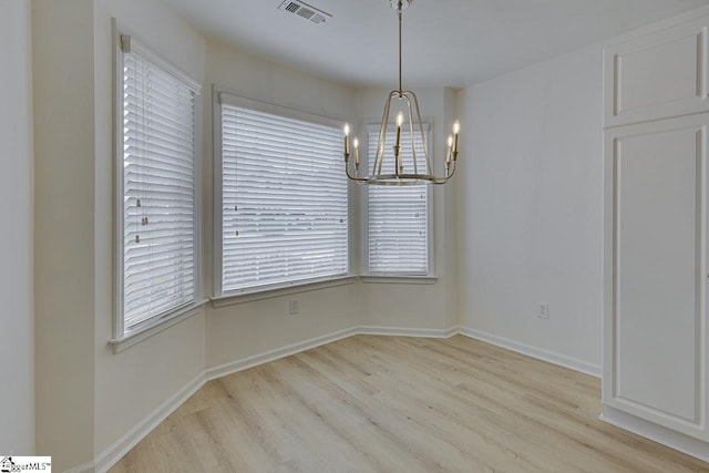 unfurnished dining area featuring a chandelier, light wood finished floors, and baseboards