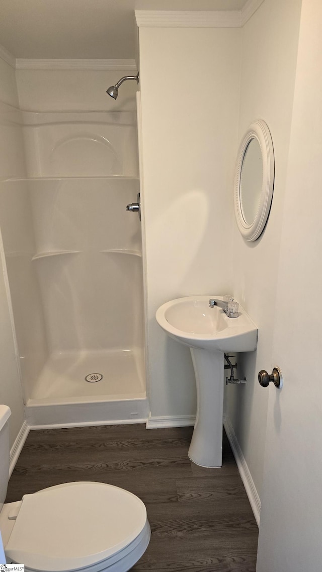 full bathroom featuring a shower stall, wood finished floors, toilet, baseboards, and crown molding