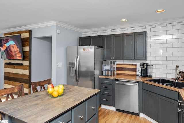 kitchen featuring stainless steel appliances, a sink, ornamental molding, butcher block counters, and light wood-type flooring