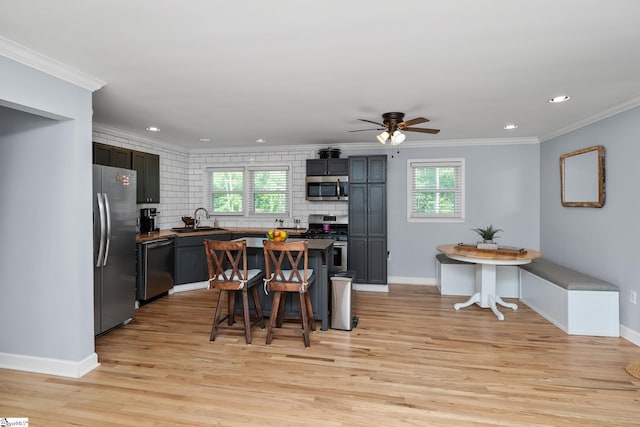 kitchen featuring appliances with stainless steel finishes, ornamental molding, light wood-type flooring, baseboards, and backsplash