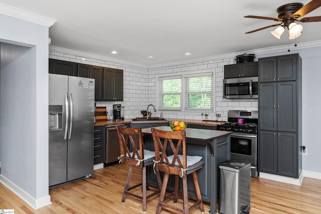 kitchen with appliances with stainless steel finishes, ornamental molding, decorative backsplash, ceiling fan, and light wood-type flooring