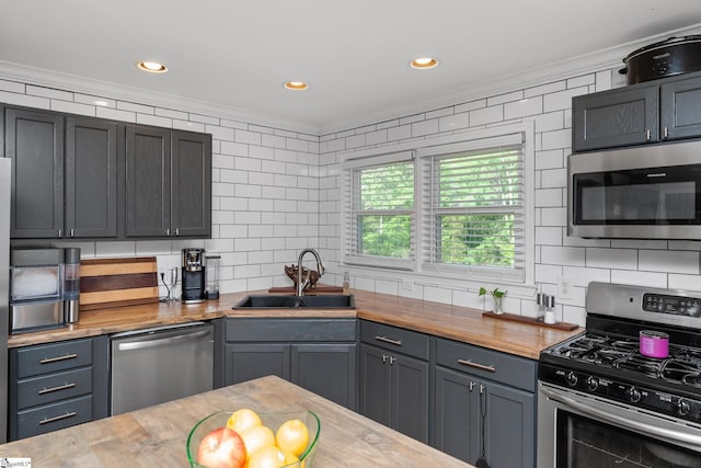 kitchen featuring stainless steel appliances, crown molding, wood counters, a sink, and tasteful backsplash