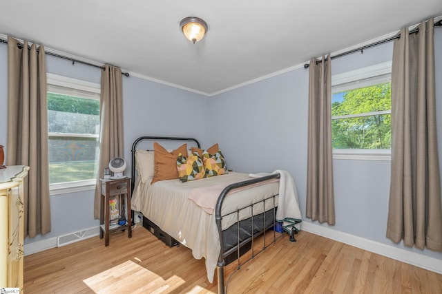 bedroom featuring baseboards, wood finished floors, ornamental molding, and multiple windows