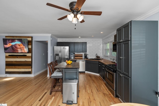 kitchen with appliances with stainless steel finishes, dark countertops, a sink, a breakfast bar, and light wood-style flooring