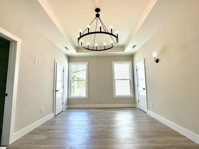 unfurnished room featuring a raised ceiling, a chandelier, wood finished floors, and baseboards