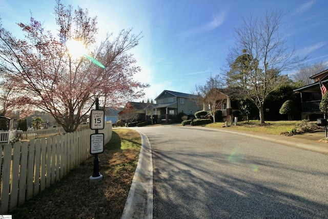view of asphalt road featuring curbs, a residential view, street lights, and sidewalks