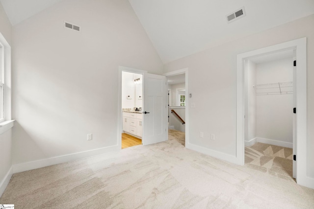 unfurnished bedroom with light colored carpet, a walk in closet, a closet, baseboards, and high vaulted ceiling