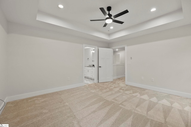 unfurnished bedroom with a raised ceiling, light colored carpet, recessed lighting, baseboards, and connected bathroom