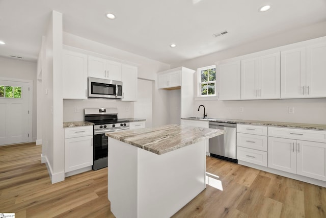 kitchen featuring appliances with stainless steel finishes, white cabinets, light stone counters, light wood-style flooring, and recessed lighting