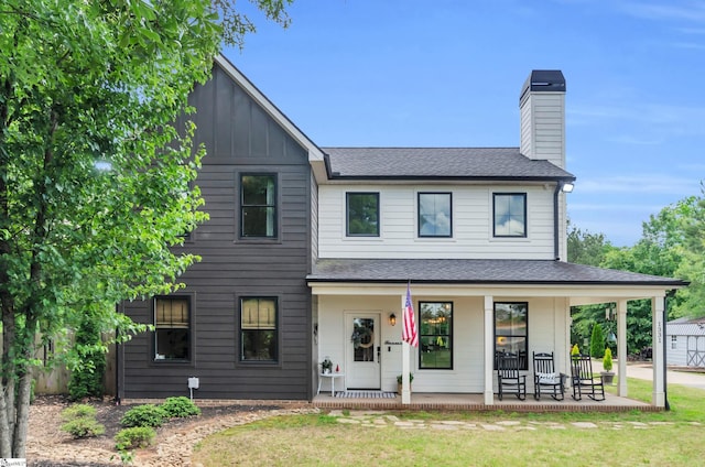 view of front of home featuring a porch, a chimney, a shingled roof, board and batten siding, and a front lawn