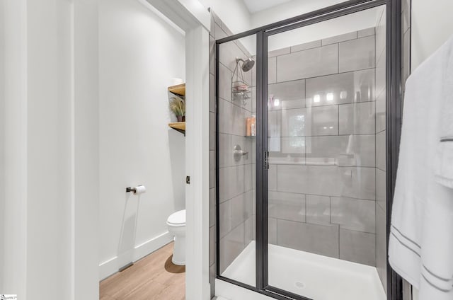full bath featuring a stall shower, toilet, wood finished floors, and baseboards