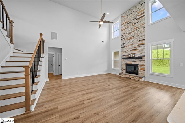unfurnished living room featuring a towering ceiling, a ceiling fan, stairway, light wood finished floors, and baseboards