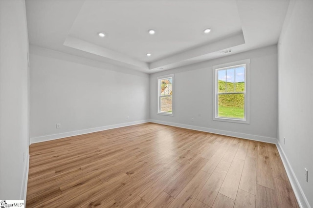 spare room featuring a raised ceiling, light wood-style flooring, baseboards, and recessed lighting