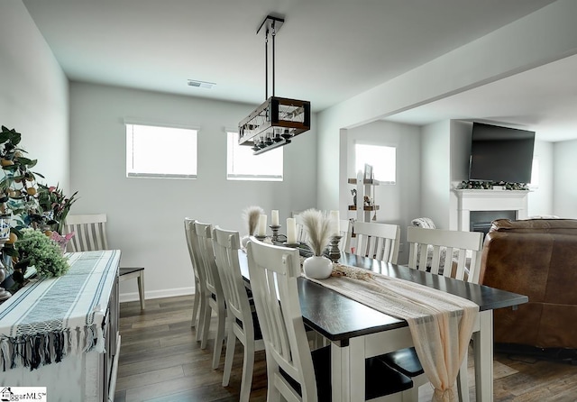 dining room featuring dark wood-style floors, plenty of natural light, a fireplace, and baseboards