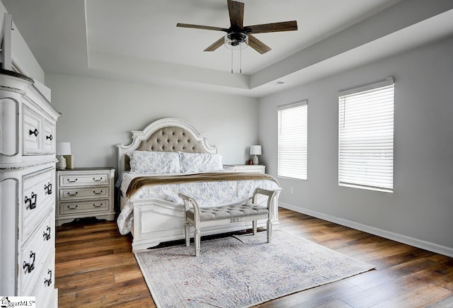 bedroom featuring a tray ceiling, dark wood-style floors, baseboards, and a ceiling fan