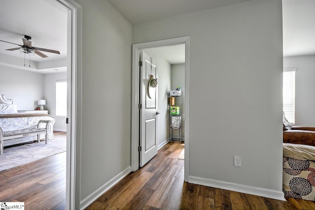 hall with dark wood-style floors, baseboards, and a raised ceiling