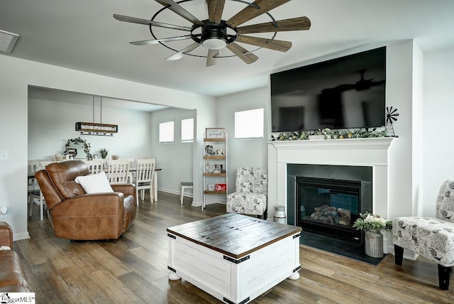 living room featuring wood finished floors, a glass covered fireplace, a ceiling fan, and baseboards
