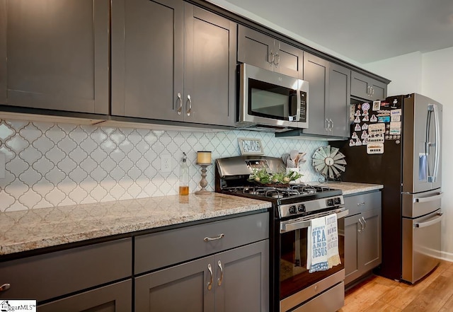 kitchen featuring appliances with stainless steel finishes, light wood-style floors, backsplash, and light stone countertops