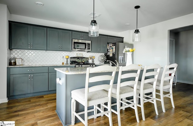 kitchen with stainless steel appliances, a kitchen island with sink, tasteful backsplash, and light countertops