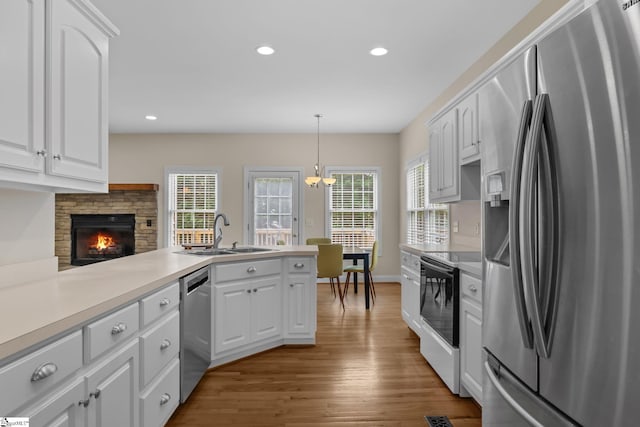 kitchen featuring stainless steel appliances, a sink, a peninsula, wood finished floors, and white cabinetry