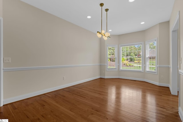 spare room featuring wood finished floors, recessed lighting, baseboards, and a chandelier