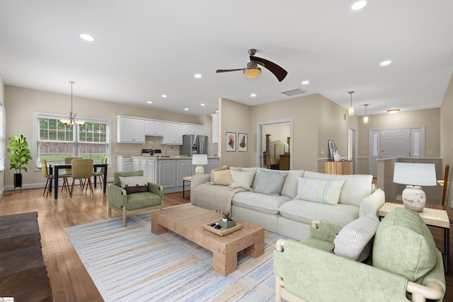 living room featuring ceiling fan, light wood finished floors, recessed lighting, a chandelier, and baseboards