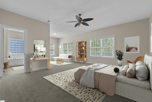 bedroom with light colored carpet, multiple windows, ensuite bathroom, and a ceiling fan