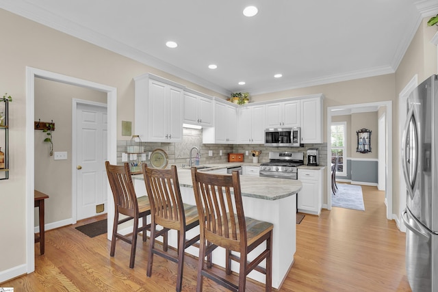 kitchen featuring stainless steel appliances, a sink, decorative backsplash, white cabinets, and ornamental molding