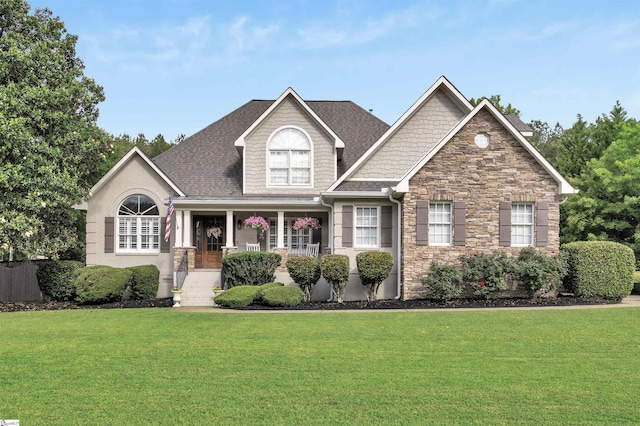 craftsman-style house featuring a front lawn, stone siding, a porch, and roof with shingles