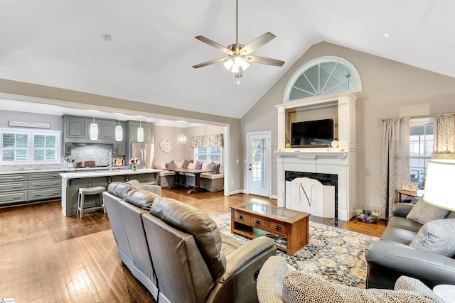 living area featuring ceiling fan, high vaulted ceiling, a fireplace, and wood finished floors
