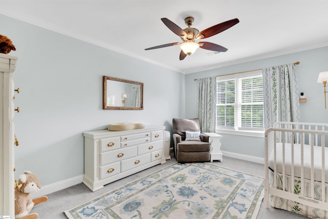 bedroom featuring baseboards, crown molding, light carpet, ceiling fan, and a crib