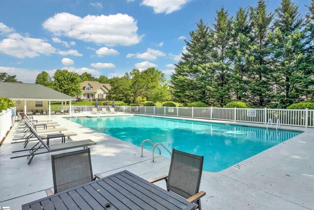 community pool with a patio, fence, and view of scattered trees