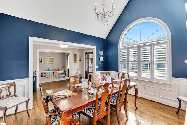 dining room with a wainscoted wall, a chandelier, a decorative wall, light wood-type flooring, and lofted ceiling