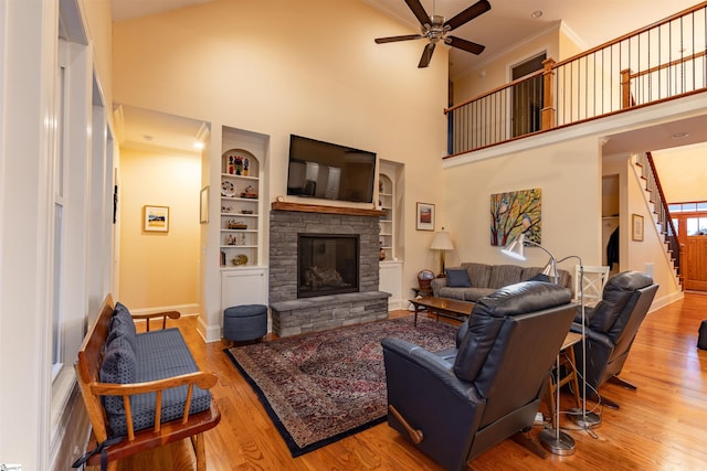 living area featuring stairs, a ceiling fan, a stone fireplace, wood finished floors, and ornamental molding