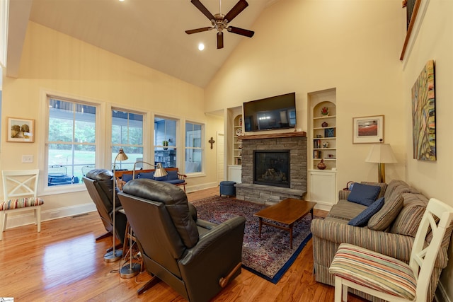living area with high vaulted ceiling, built in shelves, ceiling fan, wood finished floors, and a stone fireplace
