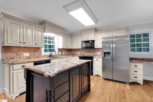 kitchen featuring black appliances, light wood finished floors, light stone counters, decorative backsplash, and a sink