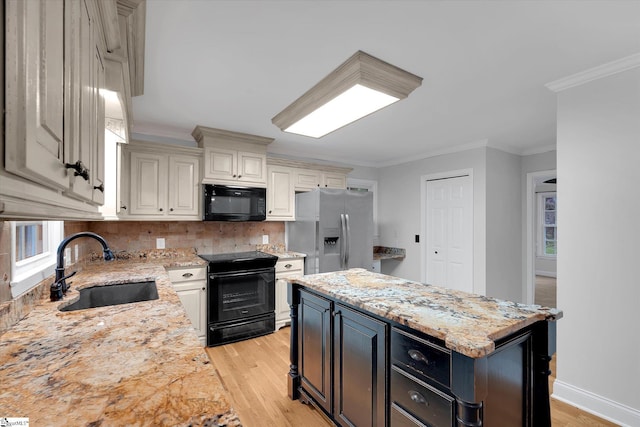 kitchen featuring black appliances, a sink, light wood-style flooring, decorative backsplash, and light stone counters