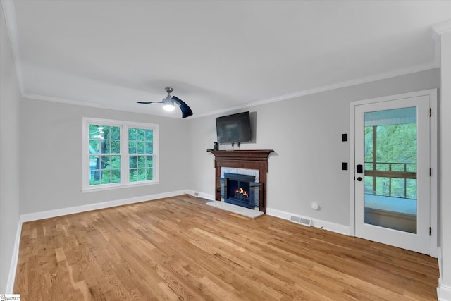 unfurnished living room with a ceiling fan, light wood-type flooring, crown molding, baseboards, and a lit fireplace