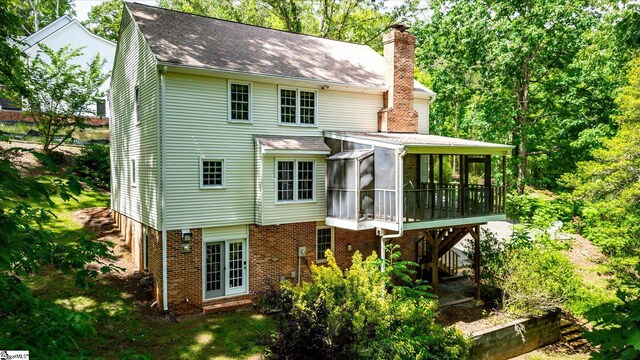 rear view of house featuring a sunroom, a chimney, brick siding, and roof with shingles