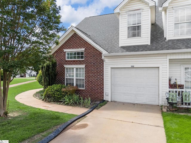 view of front of home featuring roof with shingles, driveway, brick siding, a front yard, and a garage