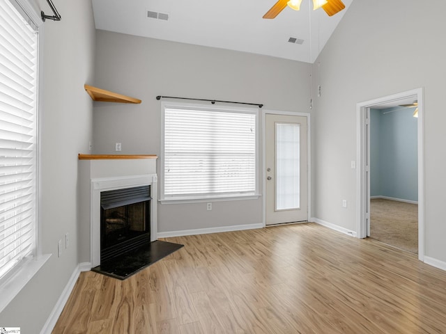 unfurnished living room featuring a ceiling fan, light wood-type flooring, a fireplace with raised hearth, baseboards, and high vaulted ceiling