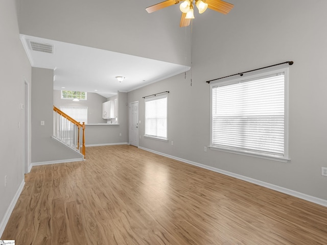 unfurnished living room with light wood finished floors, a ceiling fan, baseboards, ornamental molding, and stairway