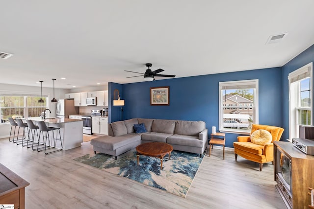 living room with healthy amount of natural light, light wood-style flooring, a ceiling fan, recessed lighting, and baseboards
