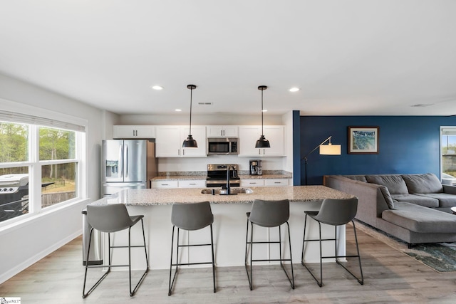 kitchen with stainless steel appliances, a sink, plenty of natural light, an island with sink, and recessed lighting