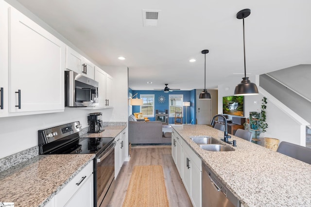 kitchen featuring stainless steel appliances, a sink, ceiling fan, light wood-style flooring, and open floor plan