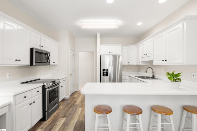 kitchen with stainless steel appliances, a sink, a kitchen bar, recessed lighting, and white cabinetry