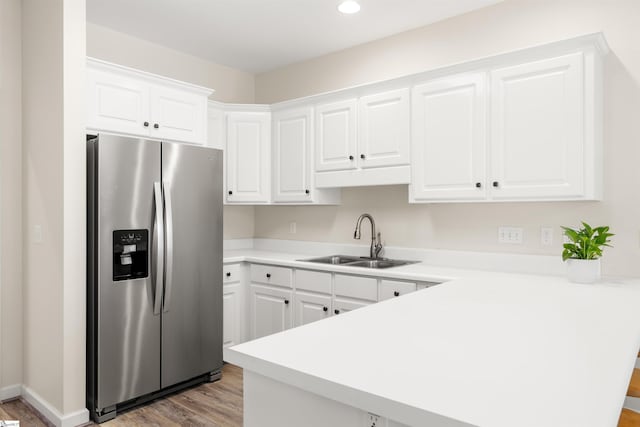kitchen featuring stainless steel fridge with ice dispenser, a sink, a peninsula, light wood-style flooring, and light countertops