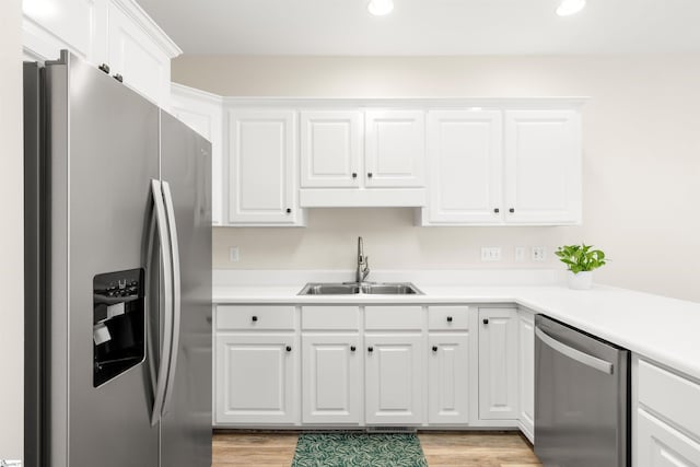 kitchen featuring appliances with stainless steel finishes, a sink, light wood-style flooring, white cabinetry, and recessed lighting