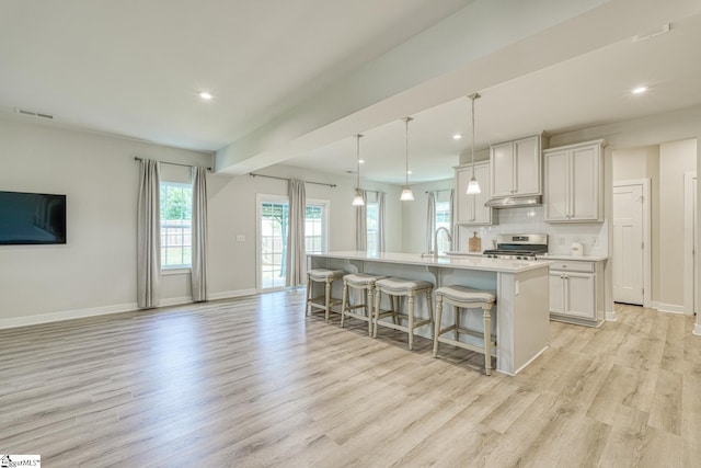 1128 Grovewood Ct, Moore, SC 29369 - kitchen featuring light wood-style flooring, under cabinet range hood, a breakfast bar area, an island with sink, and baseboards